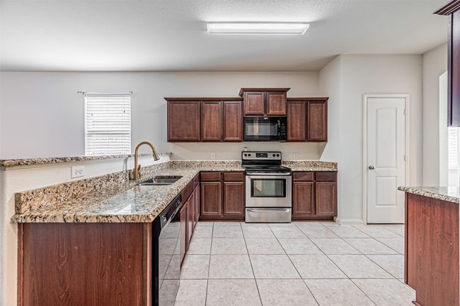 Kitchen featuring black appliances, a sink, light tile patterned floors, and light stone counters | Image 8