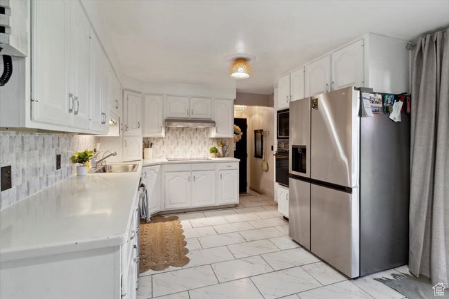 Kitchen with black appliances, light marble finish floors, white cabinetry, and under cabinet range hood | Image 5