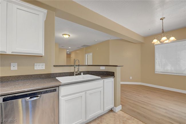 Kitchen featuring a sink, white cabinetry, dishwasher, dark countertops, and an inviting chandelier | Image 13