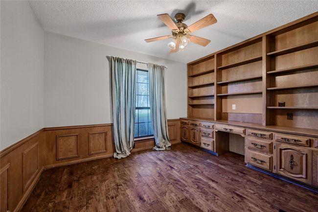 Unfurnished office with built in desk, dark wood-style flooring, a wainscoted wall, and a textured ceiling | Image 26