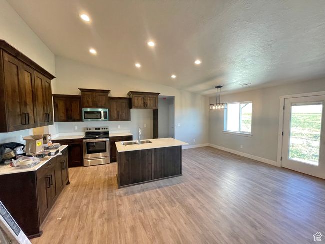 Kitchen with a sink, appliances with stainless steel finishes, dark brown cabinets, light wood finished floors, and a kitchen island with sink | Image 8