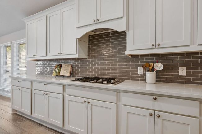 Kitchen with light stone counters, decorative backsplash, white cabinetry, and stainless steel gas cooktop | Image 6