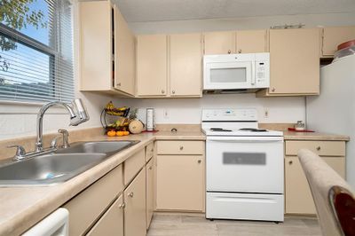 Kitchen with sink, a textured ceiling, white appliances, cream cabinetry, and light wood-type flooring | Image 3