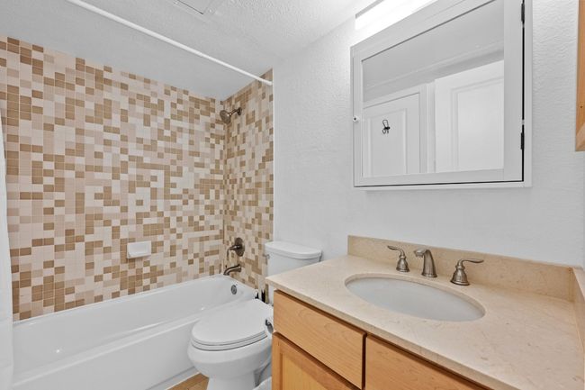 Full bathroom with toilet, vanity, tub / shower combination, a textured wall, and a textured ceiling | Image 10