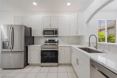 Kitchen with light stone counters, light tile floors, sink, white cabinets, and appliances with stainless steel finishes | Image 3