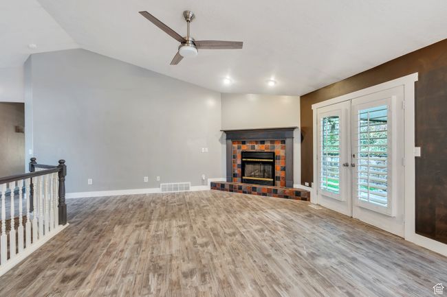 Unfurnished living room with lofted ceiling, wood finished floors, visible vents, a ceiling fan, and a glass covered fireplace | Image 8