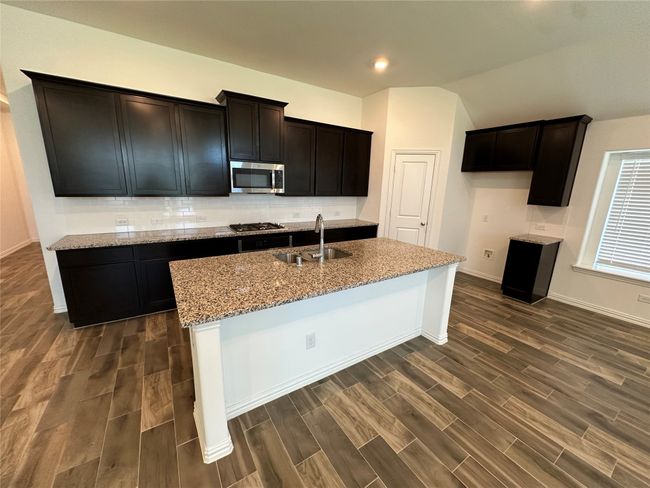 Kitchen with light stone counters, a sink, a kitchen island with sink, appliances with stainless steel finishes, and dark wood-type flooring | Image 10