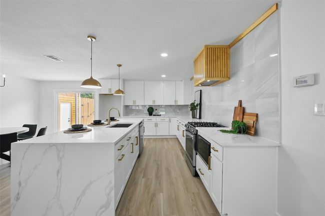 Kitchen with appliances with stainless steel finishes, a sink, tasteful backsplash, light wood finished floors, and white cabinets | Image 12