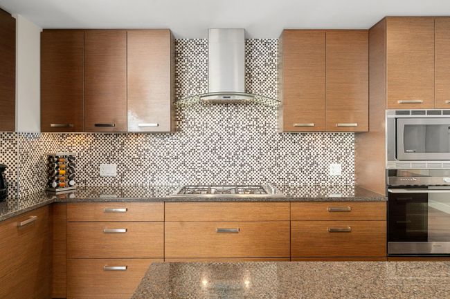 Kitchen featuring wall chimney range hood, stainless steel appliances, decorative backsplash, dark stone countertops, and modern cabinets | Image 13