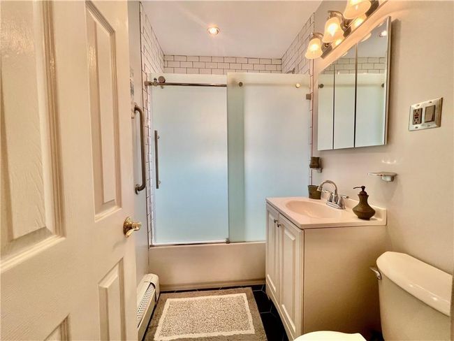 Full bathroom featuring baseboard heating, vanity, shower / bath combination with glass door, and toilet | Image 15