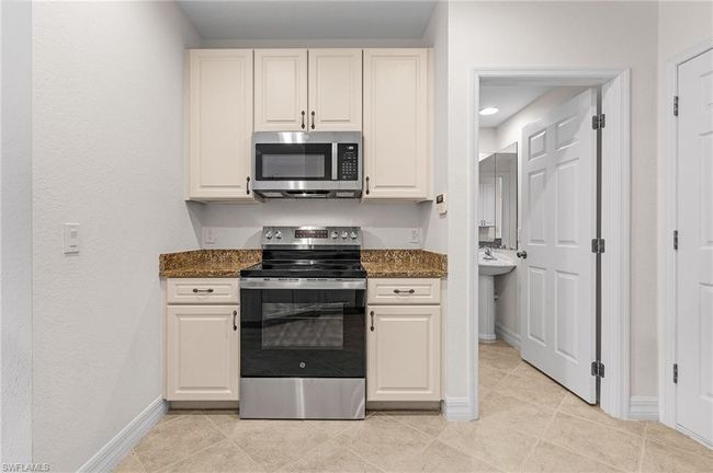 Kitchen with stainless steel appliances, light tile patterned flooring, dark stone counters, and white cabinets | Image 8