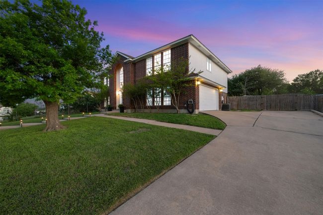 View of front facade featuring a yard, concrete driveway, fence, central air condition unit, and brick siding | Image 4