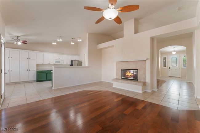 Unfurnished living room featuring a ceiling fan, light tile patterned flooring, arched walkways, a premium fireplace, and high vaulted ceiling | Image 8