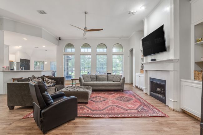 Living room featuring ceiling fan, built in features, light wood finished floors, a fireplace, and crown molding | Image 14
