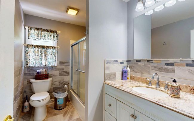Full bathroom with tile walls, toilet, vanity, tile patterned floors, and bath / shower combo with glass door | Image 23