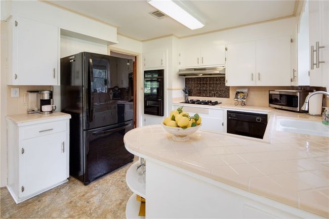 Kitchen featuring black appliances, under cabinet range hood, a sink, backsplash, and white cabinets | Image 9