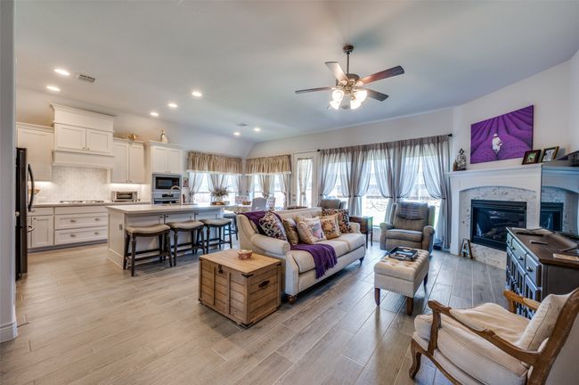 Living area featuring ceiling fan, light wood-type flooring, a stone fireplace, vaulted ceiling, and recessed lighting | Image 8