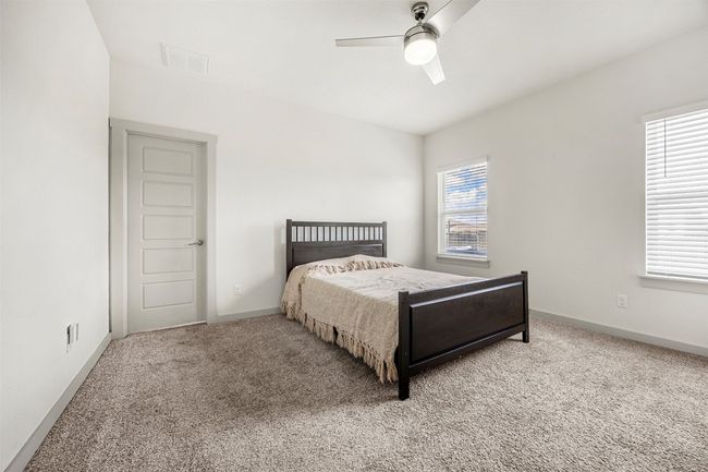 One of the three spacious bedrooms, featuring plush carpet, a ceiling fan for comfort, and large windows that provide abundant natural light. | Image 14