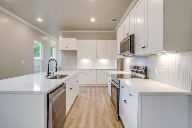Kitchen with ornamental molding, a sink, light wood finished floors, backsplash, and stainless steel appliances | Image 15