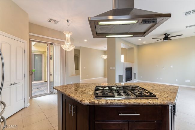 Kitchen with open floor plan, stainless steel gas stovetop, ceiling fan with notable chandelier, and visible vents | Image 6