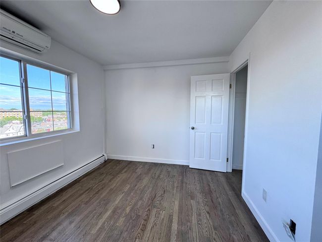 Unfurnished bedroom featuring a wall unit AC, a baseboard radiator, and dark wood-style floors | Image 9