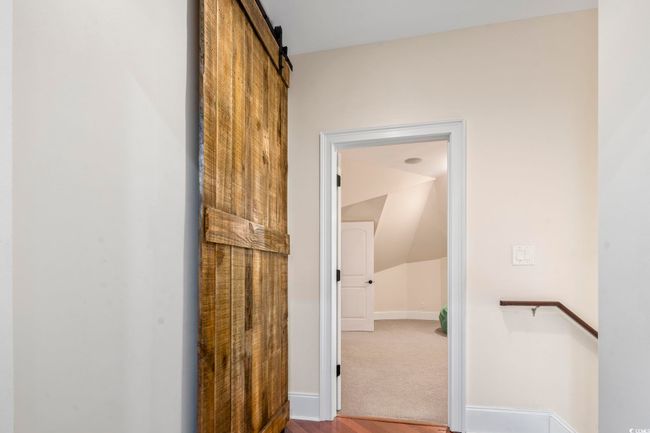 Corridor with wood finished floors, baseboards, lofted ceiling, and a barn door | Image 31
