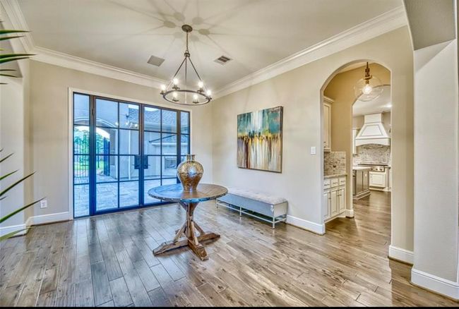 This elegant dining area features hardwood floors and a modern chandelier. Large glass doors offer a view of the patio, while an arched doorway leads to a stylish kitchen with white cabinetry. The space is accentuated by contemporary artwork and a decorative table centerpiece. | Image 8