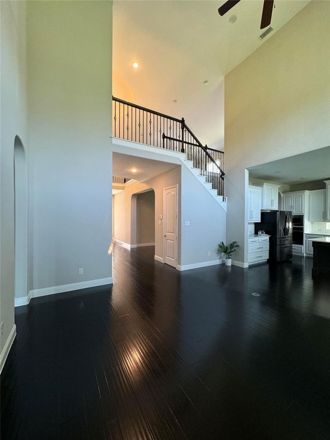 Unfurnished living room with a high ceiling, arched walkways, dark wood-style floors, ceiling fan, and stairs | Image 8