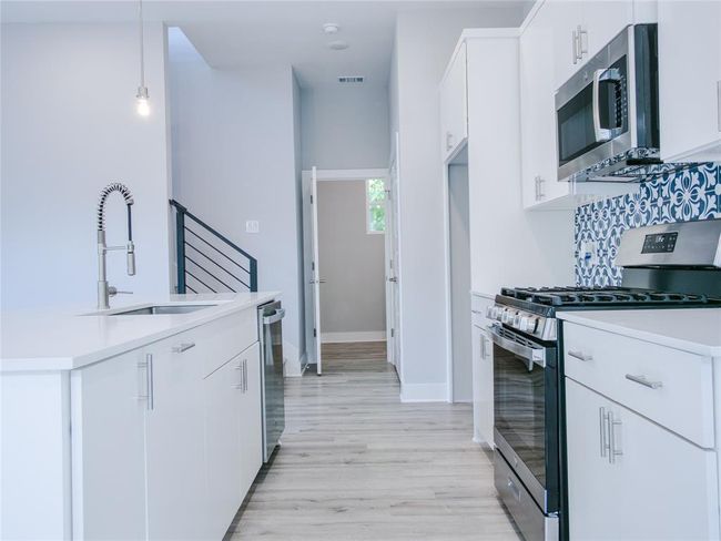 Kitchen featuring appliances with stainless steel finishes, light countertops, white cabinets, and light wood-style flooring | Image 10