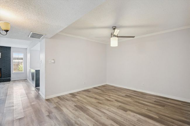 Spare room with wood finished floors, a textured ceiling, ceiling fan, a brick fireplace, and ornamental molding | Image 4