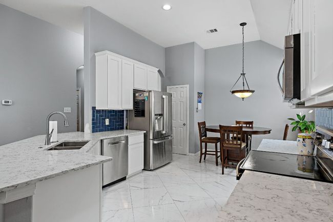 Kitchen featuring a sink, stainless steel appliances, white cabinets, light stone countertops, and light marble finish floors | Image 8