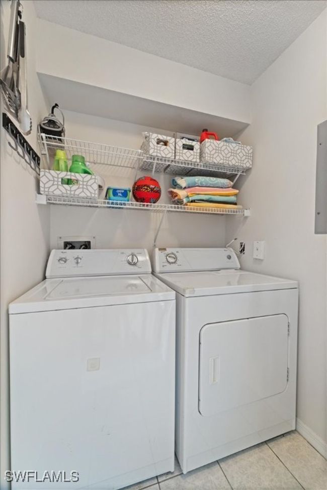 Clothes washing area featuring laundry area, a textured ceiling, light tile patterned flooring, washer and dryer, and baseboards | Image 14