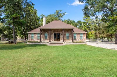 Charming single-story home with a brick facade, featuring a prominent chimney, surrounded by mature trees on a well-manicured lawn, complete with a welcoming front porch and a fenced-in property. | Image 1