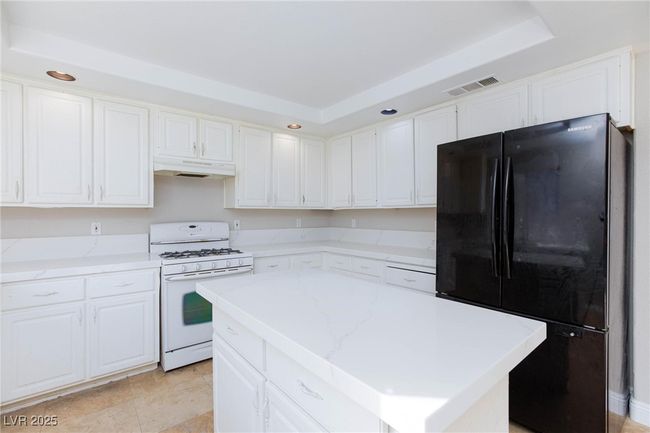Kitchen featuring freestanding refrigerator, white cabinetry, visible vents, gas range gas stove, and under cabinet range hood | Image 15