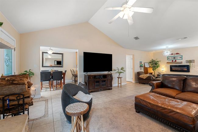 Living room featuring light tile patterned floors, ceiling fan, a glass covered fireplace, high vaulted ceiling, and baseboards | Image 14