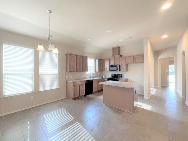 Kitchen featuring black appliances, light tile patterned floors, decorative backsplash, light countertops, and vaulted ceiling | Image 4
