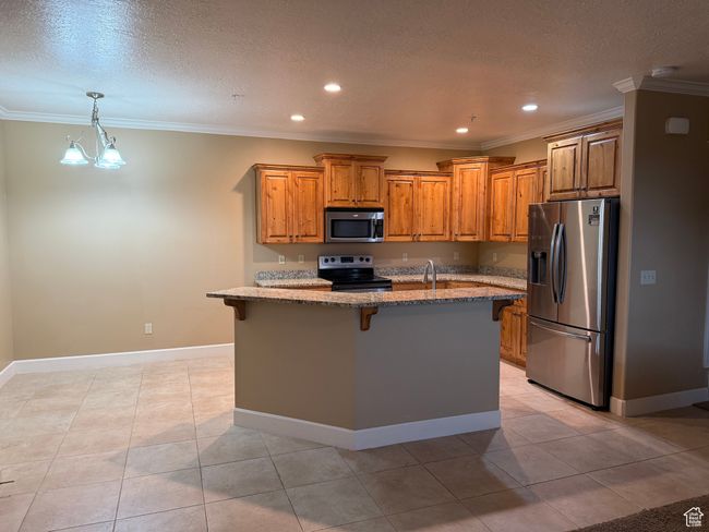 Kitchen featuring stainless steel appliances, light stone countertops, a kitchen bar, brown cabinets, and ornamental molding | Image 8