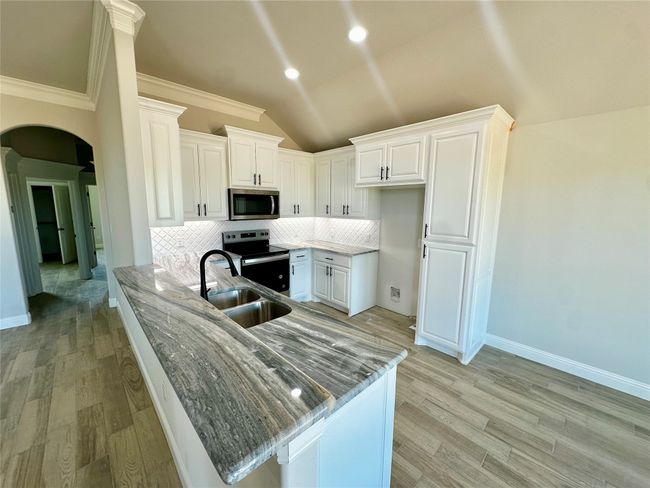Kitchen featuring stainless steel appliances, a peninsula, light wood finished floors, tasteful backsplash, and vaulted ceiling | Image 7