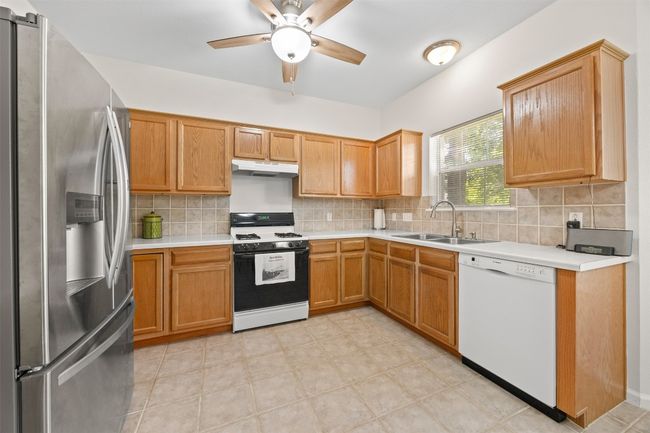 Kitchen featuring stainless steel fridge with ice dispenser, dishwasher, range with gas cooktop, under cabinet range hood, and ceiling fan | Image 11