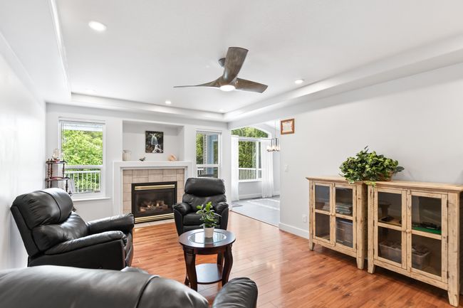 Living room featuring wood finished floors, a ceiling fan, a raised ceiling, a fireplace, and recessed lighting | Image 13