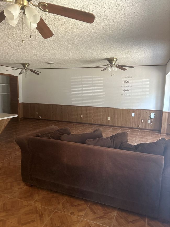 Living room with wainscoting, a textured ceiling, wood walls, and a ceiling fan | Image 4