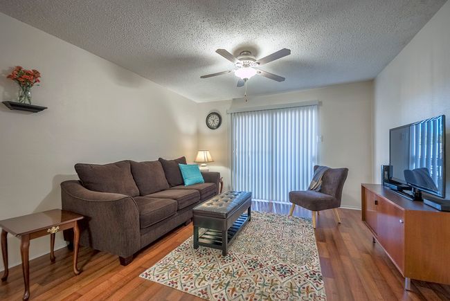 A bright living room with a comfortable couch, a stylish chair, a television, and a ceiling fan, perfect for gatherings and relaxation. | Image 6