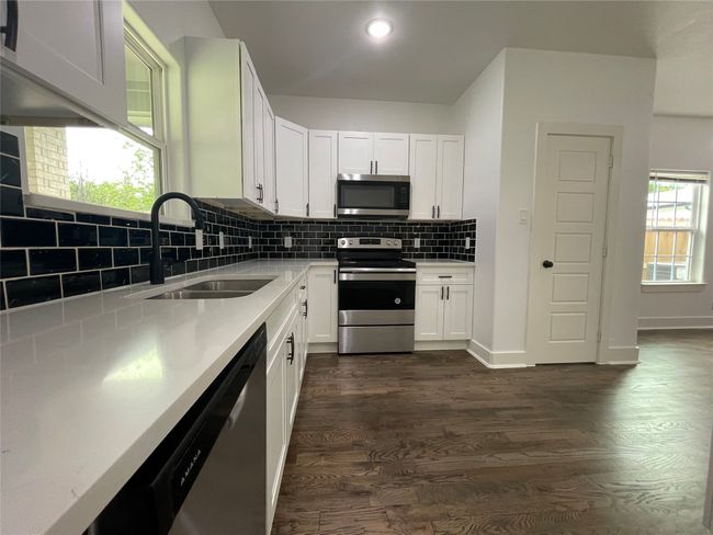 Kitchen featuring stainless steel appliances, a sink, dark wood-type flooring, decorative backsplash, and white cabinetry | Image 18