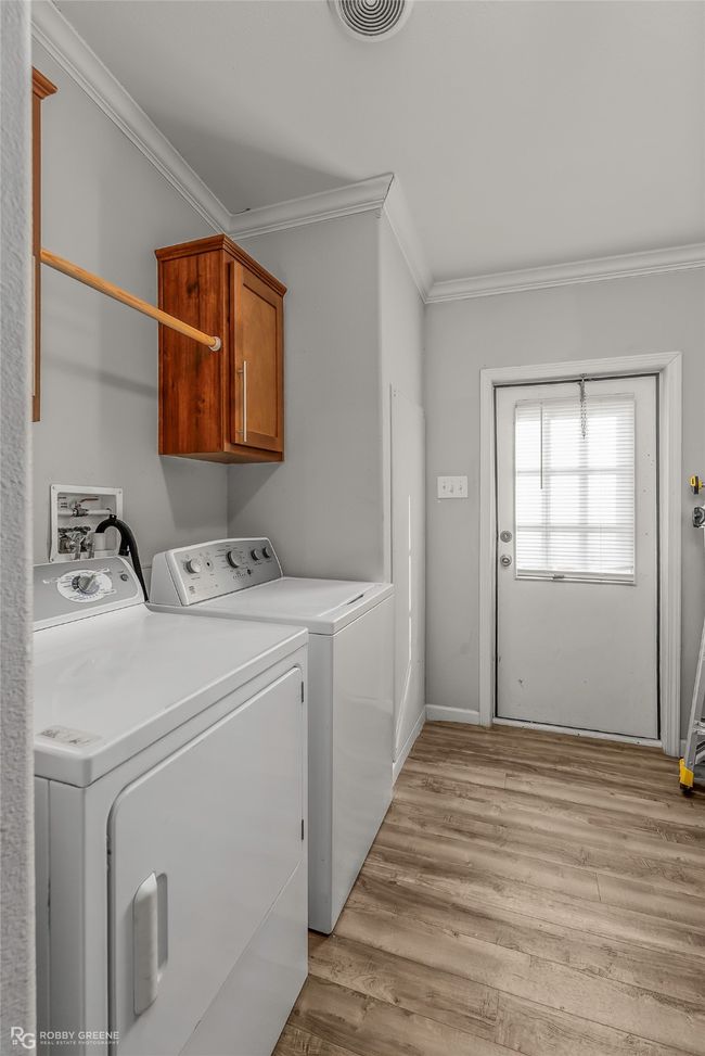 Washroom with washing machine and clothes dryer, visible vents, light wood-style floors, ornamental molding, and cabinet space | Image 35