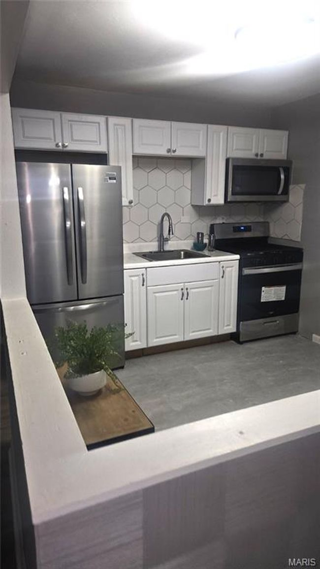 Kitchen featuring stainless steel appliances, white cabinetry, decorative backsplash, and light countertops | Image 8