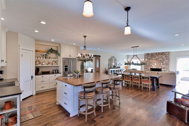 Kitchen featuring open shelves, butcher block countertops, a chandelier, white cabinetry, and stainless steel fridge | Image 9