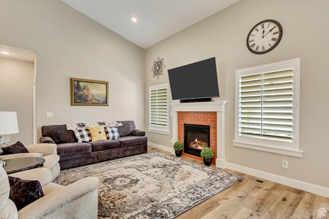 Living area with high vaulted ceiling, wood finished floors, baseboards, a brick fireplace, and visible vents | Image 6