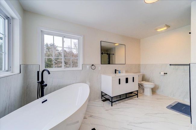 Primary en-suite bathroom featuring tile walls, a wainscoted wall, marble finish floors, a freestanding bath, and vanity | Image 24