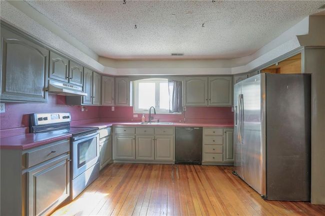 Kitchen with light wood-style flooring, visible vents, appliances with stainless steel finishes, under cabinet range hood, and a sink | Image 23