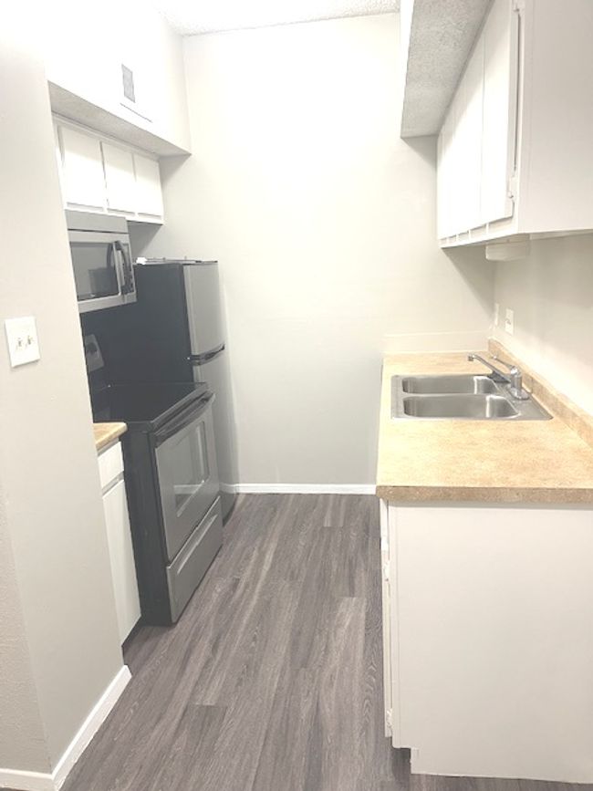 Kitchen with stainless steel appliances, a sink, white cabinetry, dark wood finished floors, and light countertops | Image 6